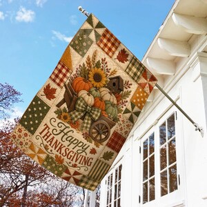 May include: A rectangular garden flag featuring a patchwork quilt design with autumn colors. The center displays a wooden wheelbarrow filled with pumpkins, sunflowers, and a birdhouse, accented by a plaid bow. The text reads Happy THANKSGIVING.