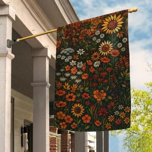May include: A rectangular garden flag hanging from a gold metal pole, featuring a stained glass style print of a dense wildflower meadow with sunflowers, daisies, and poppies in shades of orange, yellow, deep red, and dark green foliage.
