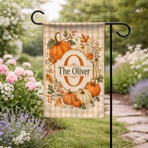 May include: A rectangular garden flag featuring a light orange and white gingham pattern. The center displays a large orange letter O with the text The Oliver inside a decorative frame, surrounded by illustrations of pumpkins and autumn leaves.