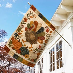May include: A rectangular decorative garden flag featuring a quilted-style design of a turkey with a colorful patterned tail, surrounded by pumpkins and autumn leaves in shades of orange, green, and brown, hanging from a metal pole mount.