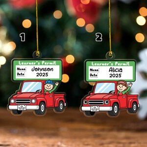 May include: Two hanging ornaments shaped like red pickup trucks with a green sign above reading Learner's Permit. The signs feature Name and Date fields with the text Johnson 2025 and Alicia 2025. Each truck has a driver and a California license plate.