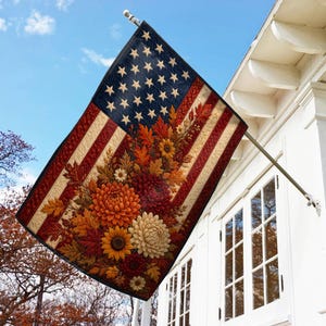 May include: A rectangular flag featuring a stylized American flag design with a dark blue canton of white stars and red and white stripes. The flag is decorated with a vibrant autumn-themed floral arrangement of orange, red, and yellow flowers.