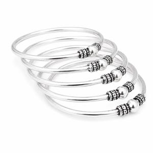 May include: A stack of five silver bangles. Each bangle is a simple, smooth band with decorative silver beads at the clasp. The beads have a textured, antique appearance. The bangles are displayed against a white background.