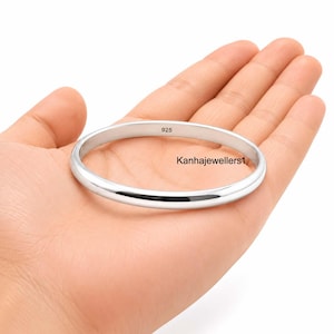 Peut inclure: Un bracelet jonc en argent poli avec une surface lisse et arrondie. L'intérieur de l'anneau porte clairement le poinçon 925, indiquant une composition en argent sterling. Le texte Kanhajewellers1 est visible sur la surface métallique.
