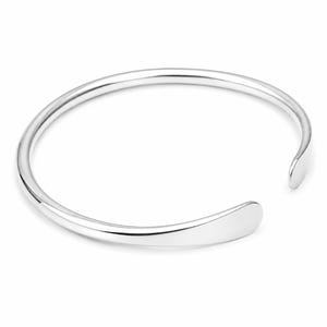 May include: A shiny silver cuff bracelet with a smooth, rounded design. The bracelet has an open design with a flat, teardrop-shaped end on one side and a rounded end on the other. The jewelry is displayed on a white background.