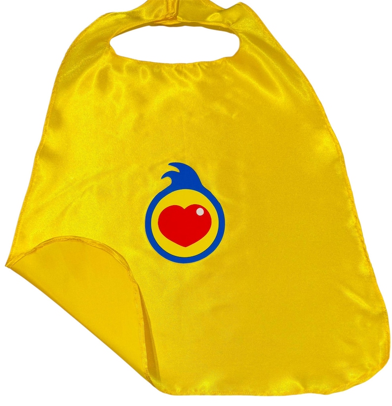 May include: A bright yellow superhero cape made of shiny fabric. The cape features a circular emblem with a red heart, a white dot, and a blue and yellow border. The cape has a neck opening and a Velcro closure.