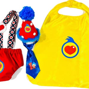 May include: A colorful baby outfit set featuring a red diaper cover, suspenders, a party hat, a blue tie, and a yellow cape. The suspenders have a white heart design. The set is designed with a heart logo.
