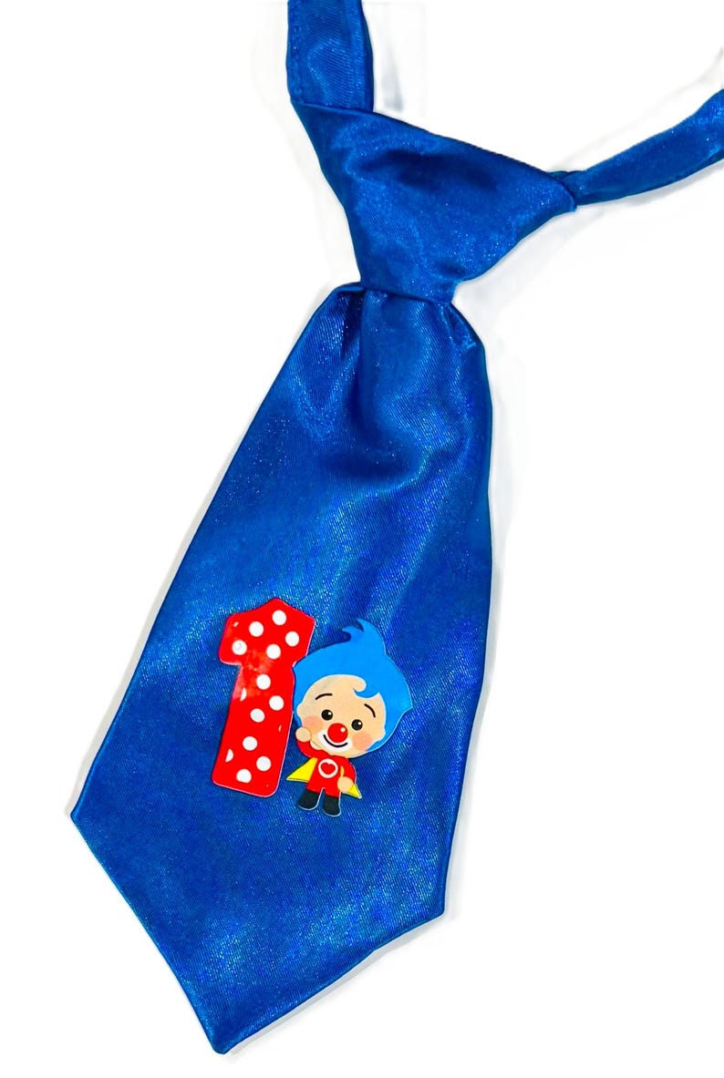 May include: A bright blue satin tie featuring a red number one with white polka dots and a cartoon character. The character has blue hair, a red nose, and a yellow cape. This tie is perfect for a child's first birthday.