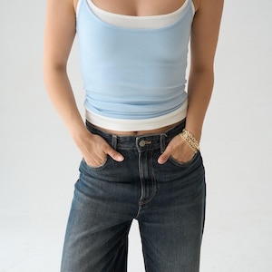 May include: A light blue ribbed tank top layered over a white tank top, paired with dark blue denim jeans. The outfit is accessorized with a white beaded necklace and a gold chain link bracelet. The text ÖA261014 Mavi is visible in the corner.