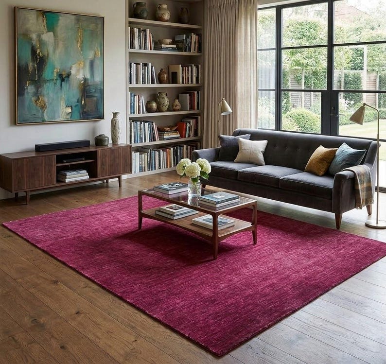 Puede incluir: Una alfombra rectangular grande de tono magenta intenso con un sutil patr&oacute;n de tejido horizontal texturizado. La alfombra est&aacute; colocada sobre un suelo de madera marr&oacute;n claro, sirviendo como base central para la disposici&oacute;n de los muebles.