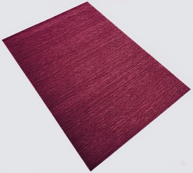 Puede incluir: Una alfombra rectangular de color magenta intenso que presenta una sutil textura lineal horizontal en toda la superficie. La alfombra se presenta desde una perspectiva en &aacute;ngulo, mostrando su color uniforme y su dise&ntilde;o de patr&oacute;n tejido consistente.