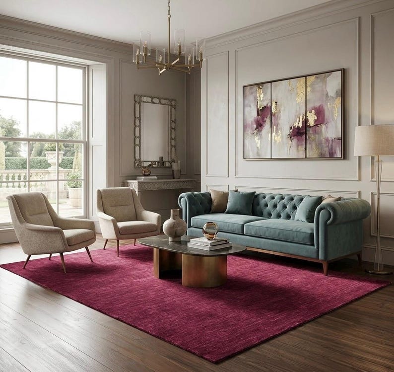 Puede incluir: Una sala de estar con un sof&aacute; capiton&eacute; color verde azulado, dos sillones beige y una alfombra color magenta oscuro. Una mesa de centro ovalada con base dorada se sit&uacute;a en el centro. Un gran cuadro abstracto de tres paneles con toques dorados y morados.
