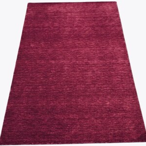 Puede incluir: Una alfombra rectangular de color magenta intenso y s&oacute;lido. La superficie presenta un sutil patr&oacute;n de tejido texturizado horizontal que crea ligeras variaciones en la intensidad del tono magenta a lo largo de toda la alfombra.