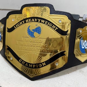 May include: A gold and black championship belt. The belt has the text "LIGHT HEAVYWEIGHT" and "WORLD WRESTLING FEDERATION CHAMPION". It features a gold center plate with a blue globe and the WWF logo on the side plates.