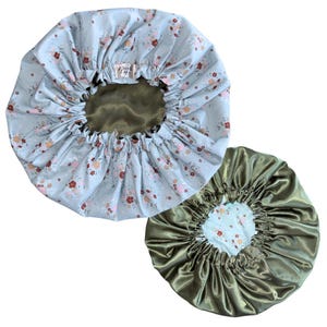 May include: Two reversible hair bonnets with an elasticized gathered edge. One side features a light blue fabric with a small floral pattern in red, pink, and white. The other side is a solid olive green satin fabric. A small label reads "Silk Life".