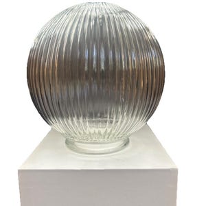 May include: A spherical clear glass light shade featuring a vertical ribbed texture throughout its surface. The globe has a circular opening at the base with a smooth rim, designed for attachment to a lighting fixture, presented as a single unit.
