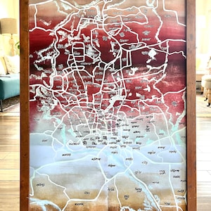 May include: A framed map of a city with white lines and black text on a red, orange, and brown background. The map is titled "Dhaka" in the top left corner.