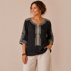 May include: A black blouse featuring a split neckline and three-quarter length sleeves, adorned with intricate gold-toned geometric embroidery along the collar, front placket, and sleeve cuffs, paired with light beige wide-leg trousers.