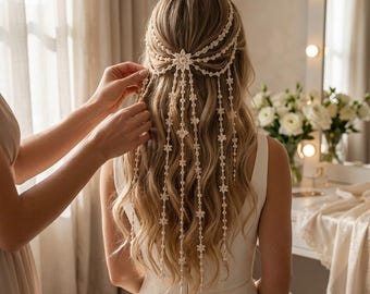 Puede incluir: Un accesorio para el cabello de color crema con un motivo central en forma de estrella y múltiples hilos en cascada adornados con pequeñas cuentas en forma de flor, dispuestos sobre el cabello largo y ondulado con un efecto decorativo.