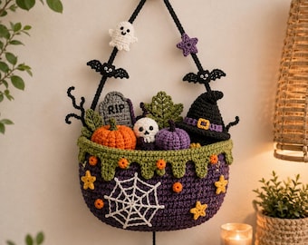 Puede incluir: Una cesta de pared tejida a ganchillo en color morado con una telaraña blanca, estrellas naranjas y amarillas, y un patrón de goteo verde. Contiene una calabaza, una calavera, una lápida con el texto RIP y un sombrero de bruja tejidos.