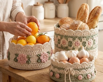 Puede incluir: Tres cestas redondas de ganchillo con bordes festoneados y motivos florales. Una cesta contiene naranjas y limones, otra barras de pan y la tercera bulbos de ajo y cebollas. Las cestas están hechas con hilo de color crema, verde salvia y rosa.