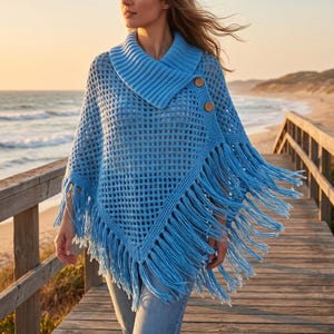 May include: A light blue crochet poncho featuring an open grid pattern, a wide ribbed fold-over collar, and two large wooden buttons on the side. The garment is finished with long, dangling fringe along the bottom hem, creating a textured look.