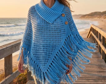 Puede incluir: Un poncho de ganchillo azul claro con un patrón de rejilla abierta, un cuello ancho de canalé y dos botones grandes de madera en el lateral. La prenda está rematada con largos flecos colgantes a lo largo del dobladillo inferior, creando un aspecto texturizado.