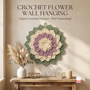 Puede incluir: Un tapiz de pared de flor de ganchillo circular con pétalos en capas en color crema, morado y verde salvia. El texto CROCHET FLOWER WALL HANGING Digital Crochet Pattern PDF Download aparece sobre la pieza de arte textil.