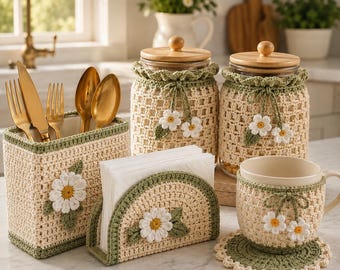 May include: A set of kitchen accessories featuring cream and sage green crochet covers with white daisy appliqués. The set includes a rectangular utensil holder with gold cutlery, two glass jars with wooden lids, a napkin holder, and a mug with a coaster.