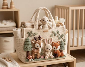 Puede incluir: Un bolso de ganchillo beige con aplicaciones tridimensionales de peluche de un ciervo, un conejo y un zorro, junto con árboles verdes y una seta. Un pequeño cordero de ganchillo se encuentra dentro del bolso, que también contiene una manta.