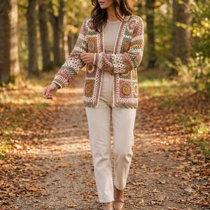 May include: A long-sleeve cardigan made of crocheted granny squares in shades of cream, sage green, dusty pink, and mustard yellow. The open-front garment is worn over a plain cream-colored top and paired with cream-colored trousers.