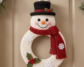 May include: A crocheted snowman wreath featuring a black top hat with a red band and holly, a cream-coloured head with an orange nose, and a red scarf. The circular body is cream-coloured with white snowflake appliques and green holly leaves.