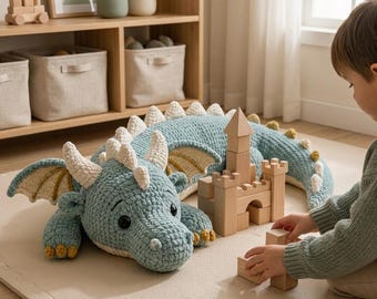 Puede incluir: Un gran dragón de peluche tejido a ganchillo en color azul claro con cuernos, espinas y detalles en las alas de color crema. El dragón presenta ojos de seguridad negros y un acabado de hilo texturizado, junto a un castillo de bloques.