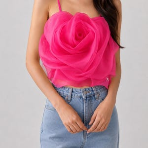 Pu&ograve; includere: Un top camisole rosa acceso con un grande design a rosa tridimensionale. Il top ha sottili spalline e viene abbinato a jeans di denim blu chiaro. La rosa &egrave; il punto focale, creando una dichiarazione floreale audace.