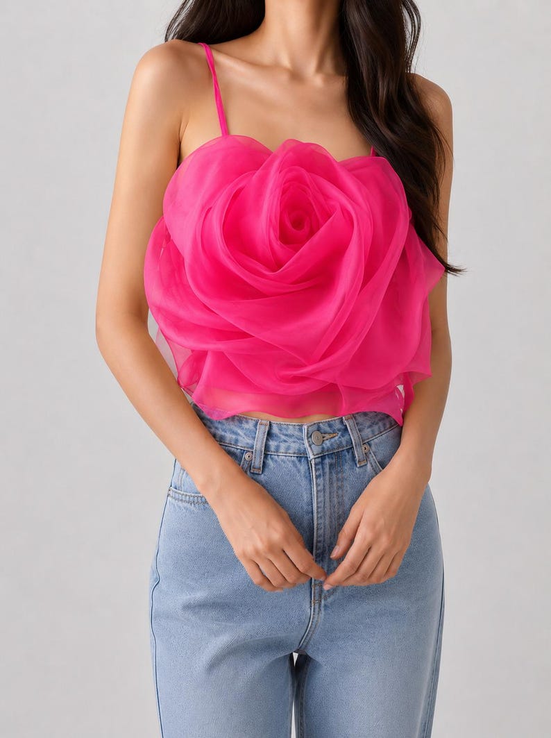 Pu&ograve; includere: Un top camisole rosa acceso con un grande design a rosa tridimensionale. Il top ha sottili spalline e viene abbinato a jeans di denim blu chiaro. La rosa &egrave; il punto focale, creando una dichiarazione floreale audace.