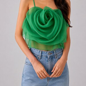 Pu&ograve; includere: Un top verde senza maniche con un grande design a rosa a strati. Il top ha sottili spalline e si abbina a jeans di denim blu chiaro. La rosa &egrave; il punto focale, realizzata in un tessuto trasparente e fluido.