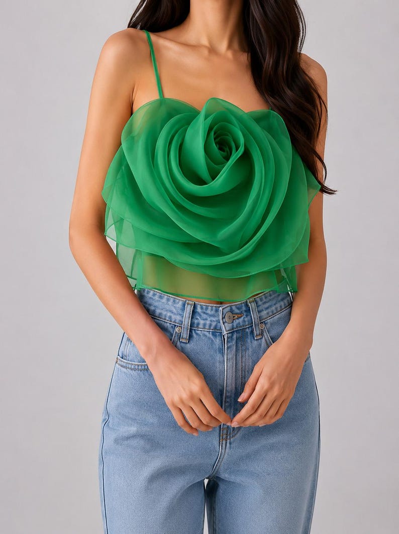 Pu&ograve; includere: Un top verde senza maniche con un grande design a rosa a strati. Il top ha sottili spalline e si abbina a jeans di denim blu chiaro. La rosa &egrave; il punto focale, realizzata in un tessuto trasparente e fluido.