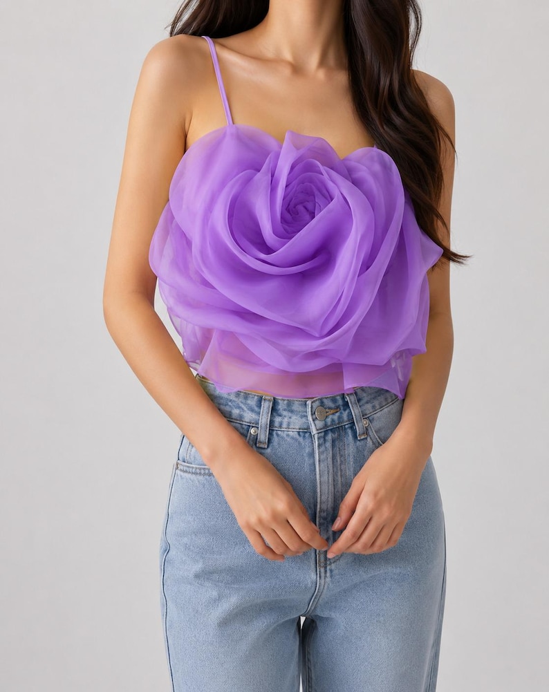 Pu&ograve; includere: Un top a camisole color lavanda con un grande design a rosa tridimensionale. Il top ha sottili spalline e viene abbinato a jeans di denim blu chiaro. La rosa &egrave; il punto focale, creando un look unico e accattivante.