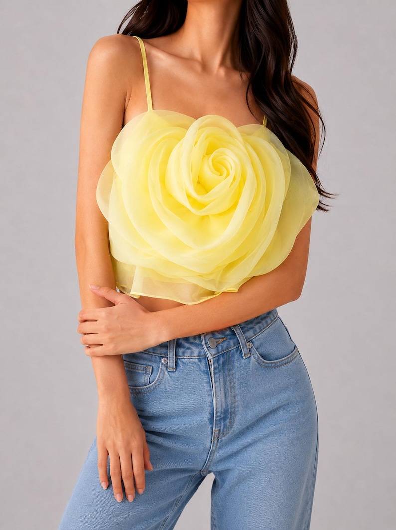 Pu&ograve; includere: Un top corto giallo con un grande design a rosa a strati. Il top ha sottili spalline e viene abbinato a jeans di denim blu chiaro. La rosa &egrave; il punto focale, creando una dichiarazione floreale audace.