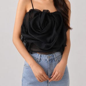 Pu&ograve; includere: Top a camisole nero con un grande design a rosa arricciata. Il top presenta sottili spalline e viene abbinato a jeans di denim blu chiaro. Il design a rosa &egrave; il punto focale, creando un look unico ed elegante.