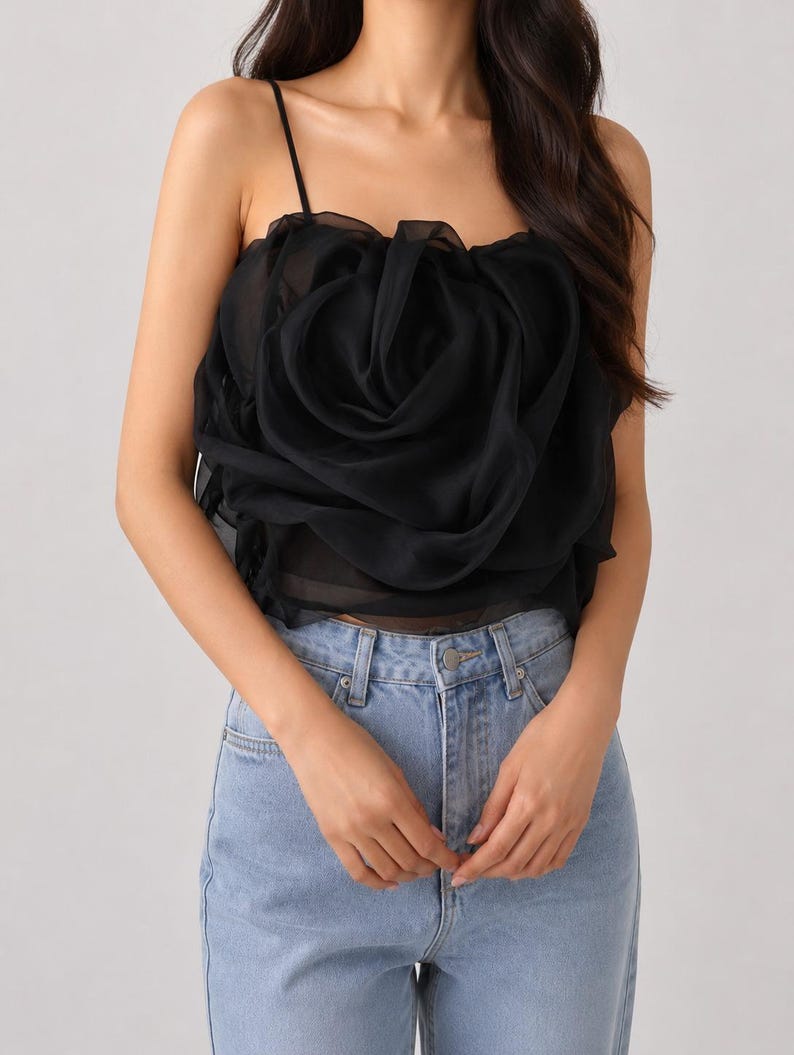 Pu&ograve; includere: Top a camisole nero con un grande design a rosa arricciata. Il top presenta sottili spalline e viene abbinato a jeans di denim blu chiaro. Il design a rosa &egrave; il punto focale, creando un look unico ed elegante.