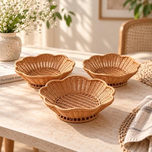 May include: Three light brown woven baskets with a scalloped edge design. Each basket features a circular base and a shallow, open bowl shape constructed from thin, flexible material. The baskets are arranged in a cluster on a flat surface.