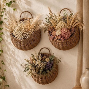 Op de afbeelding: Drie ronde, bruine wandmanden van gevlochten riet, elk voorzien van een stevig handvat om op te hangen. Deze manden zijn gevuld met arrangementen van droogbloemen, waaronder pampasgras, gipskruid, hortensia's en eucalyptusbladeren.