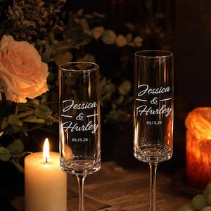 May include: Two clear glass champagne flutes featuring white etched text that reads Jessica & Hurley with the date 05.15.26. The tall, slender glasses have a smooth cylindrical bowl and a thin stem, designed for celebratory toasts and events.
