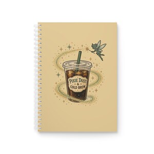 May include: A spiral-bound notebook with a tan cover featuring a graphic of a plastic cup filled with dark cold brew coffee. The cup has a green straw and text reading Pixie Dust & Cold Brew. A small fairy with wings flies nearby.