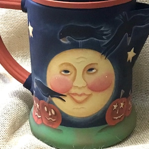 Puede incluir: Una jarra de cerámica azul y roja con un diseño de luna y cuervo. La jarra tiene las palabras "Old Crow Seed Co." en el lateral.