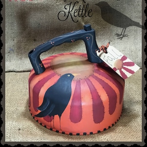 May include: A hand-painted tea kettle with a black crow and a red and orange sunburst design. The kettle has a black handle and a tag that says "Fall".