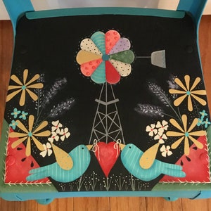 May include: A hand-painted wooden chair with a black seat featuring a whimsical scene of a windmill, two birds, and flowers. The chair is painted in shades of teal, green, and red.
