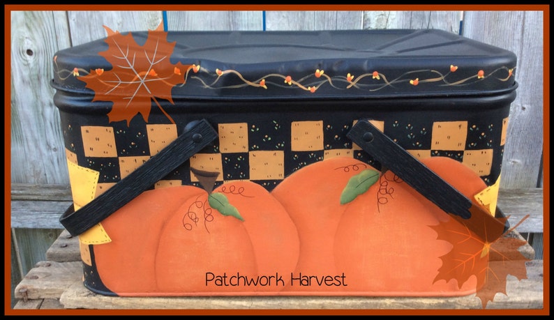 Pu&ograve; includere: Cesto da picnic in metallo nero con un motivo a scacchi e zucche dipinte. Il cesto ha due manici neri e una vite con bacche rosse dipinte sulla parte superiore. Il testo "Patchwork Harvest" &egrave; dipinto sulla parte anteriore.