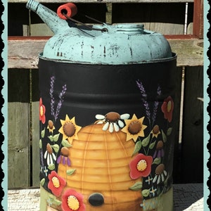 May include: A repurposed metal can with a light blue top and a black body. The body is decorated with a beehive, sunflowers, and other flowers. The words "Bee Garden" are written across the top.